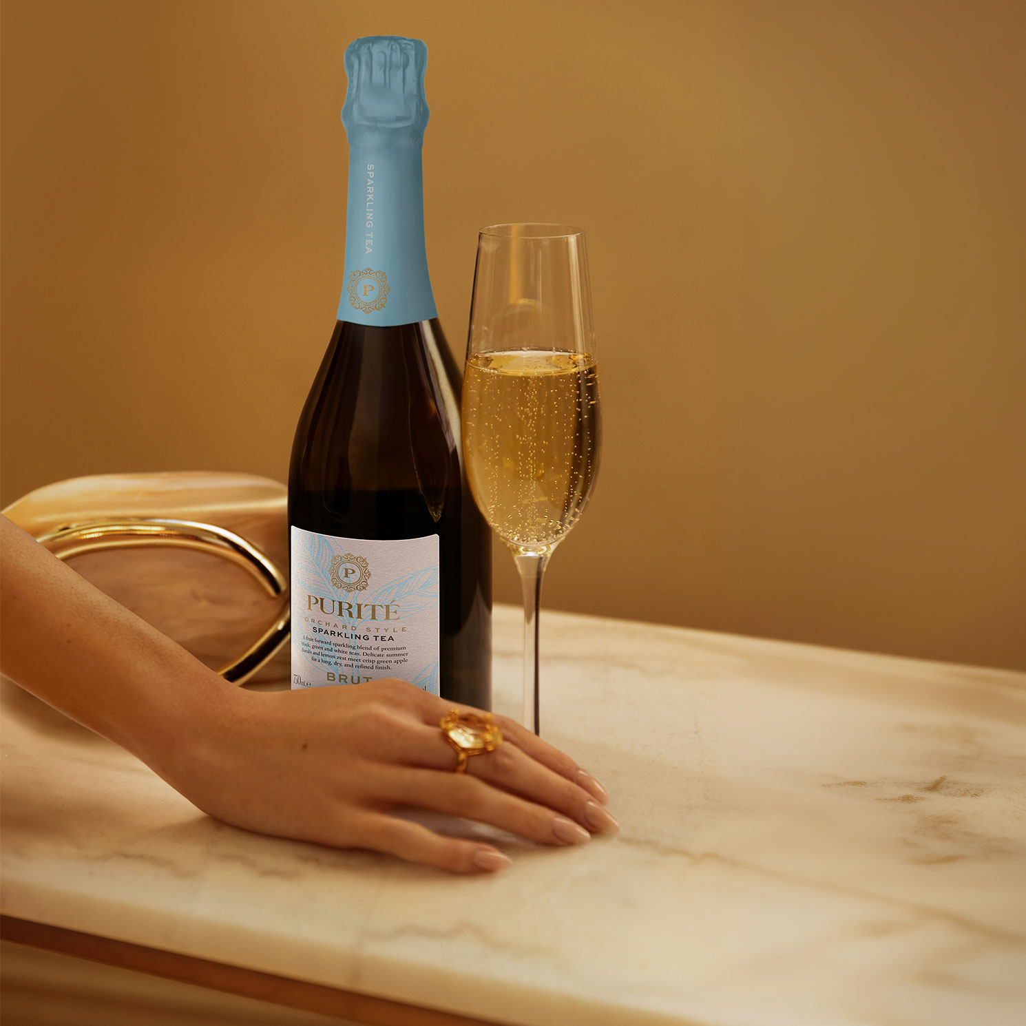 A woman's hand holding a bottle of Purité and a glass of Sparkling Tea,